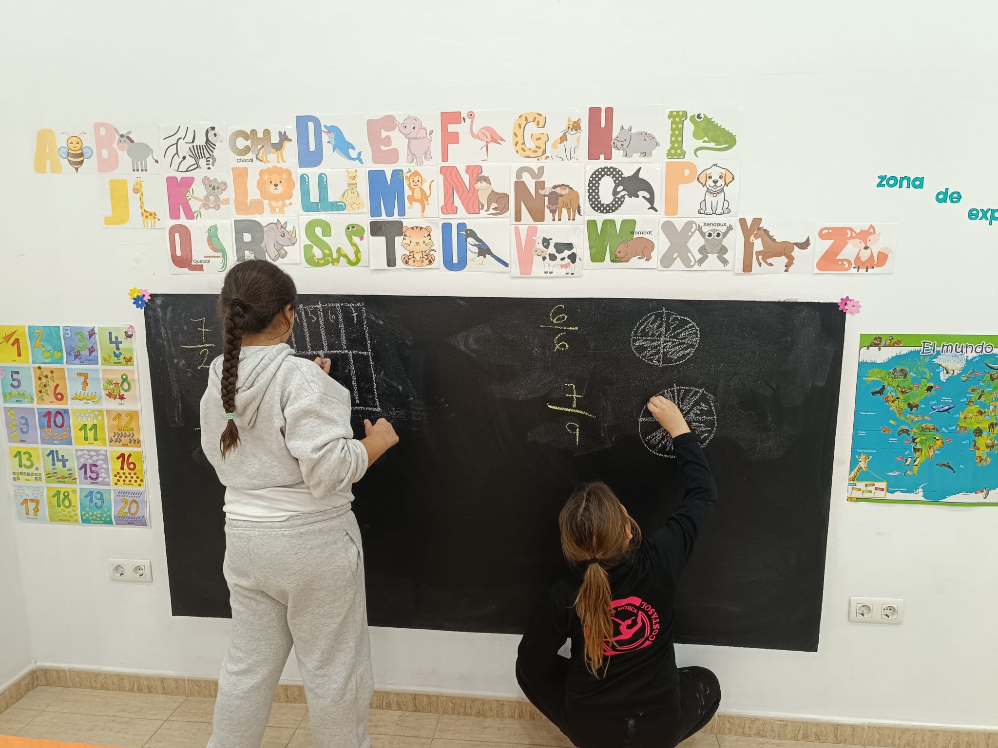 Niñas escribiendo en la pizarra junto al abecedario en una sesión de refuerzo escolar